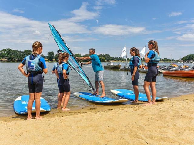 4 jeunes écoutent leur prof de planche à voile qui leur fait une démonstatrion sur la plage