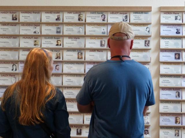 Deux visiteurs de dos, un homme et une femme regardent le mur sur lequel sont exposés tous les portraits des déportés mayennais à la Vigie - Mémorial des déportés de la Mayenne.