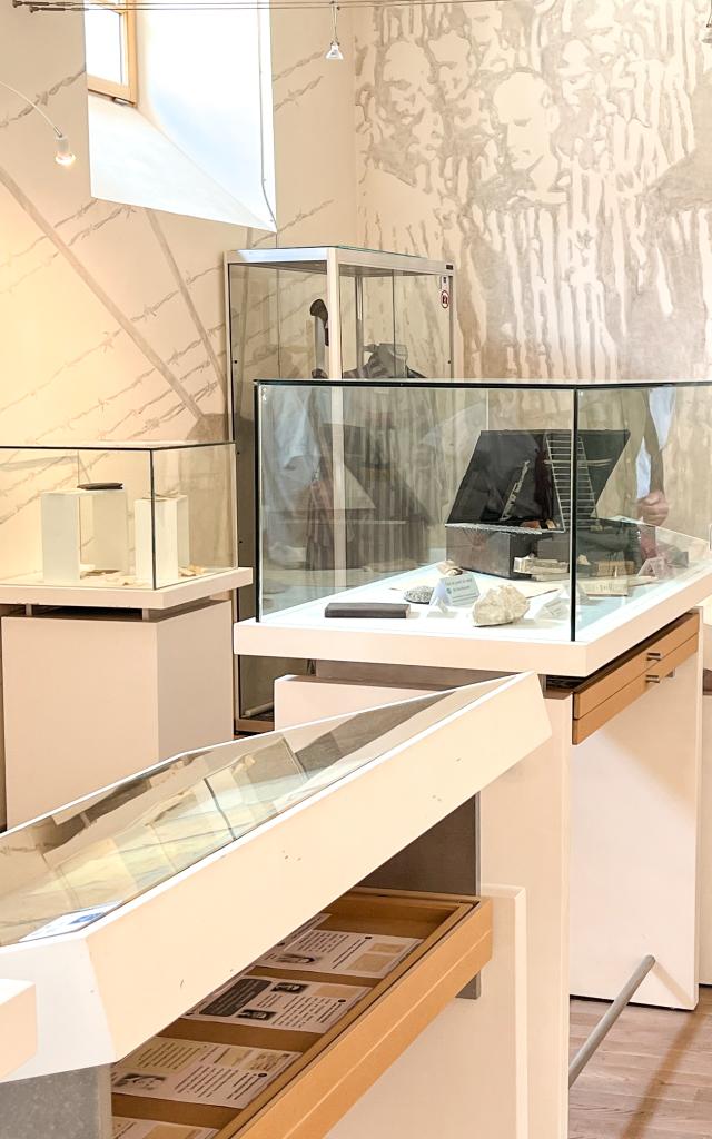 Trois visiteurs observent les objets exposés en vitrine à la Vigie - Mémorial des Déportés de la Mayenne. L'un deux est proche du photographe, de face, les deux autres sont à l'arrière plan et sont de profil.